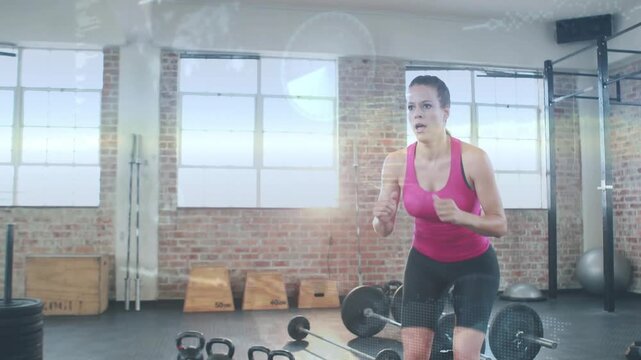 Woman pulling arms back and launching explosive jump-squats over kettlebells in gym for fitness