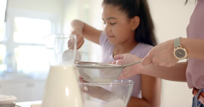 African American mom placing sieve as teenage girl pouring flour, sifting bowl for baking at home