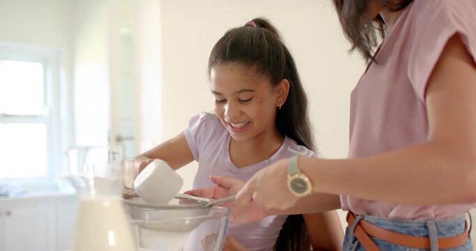 African American mother holding sieve as daughter tilting cup pouring into bowl counter for batter