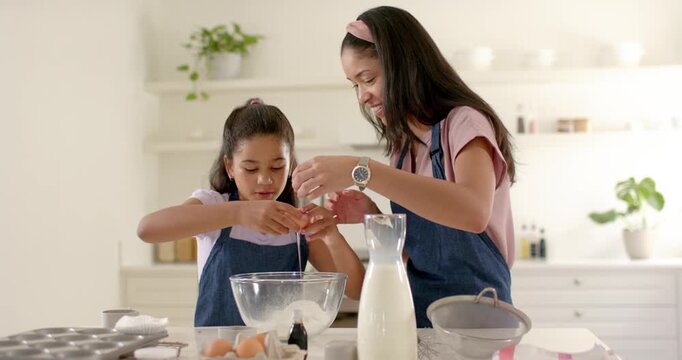 Reaching daughter cracking eggs while mother steadying bowl at home for baking, in blue aprons