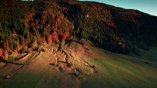 Aerial view of a valley in the Bavarian Alps illuminated by warm light at sunrise, with colorful autumn trees and orange vegetation