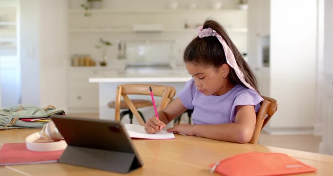 Writing student studying at home table on tablet ping tapping tablet while writing in red notebook