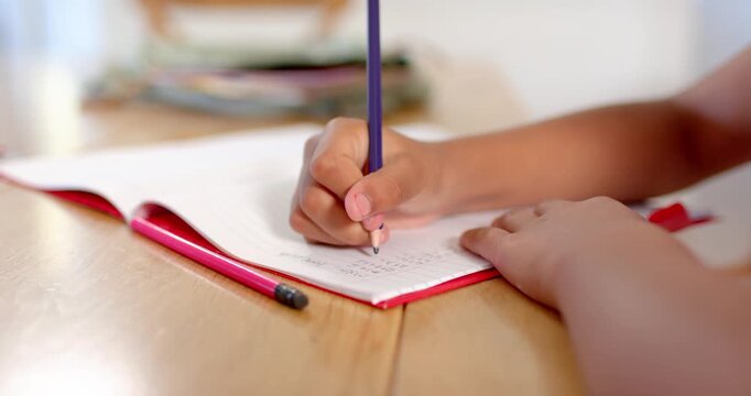 African American teen gripping purple pencil, steadying red notebook on wood table, doing homework
