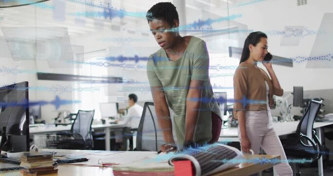 Diverse team framing African American woman in green top leaning over desk marking plans with pen
