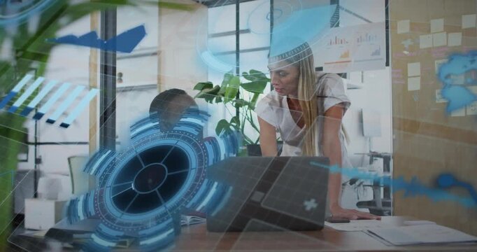 Vertical video: Two women at desk gesturing at laptop making blue UI grow while reviewing biz data