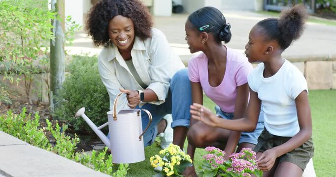 Woman with teenage and child girls planting flowers on lawn, watering with pink metal watering can