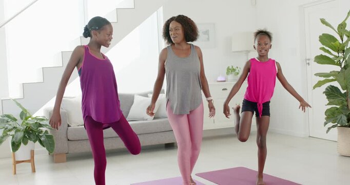 African American female family doing balance stretches on three yoga mats at home in workout gear