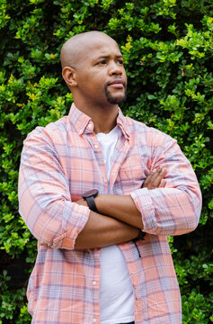 Diffused light initiating thoughtful pose, Black man standing arms crossed, showing smartwatch