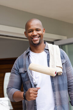 African American man standing in doorway holding paint roller, wearing white tee, towel on shoulder