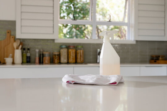 Showing spray bottle with liquid sitting on microfiber cloth on kitchen countertop with pantry jars