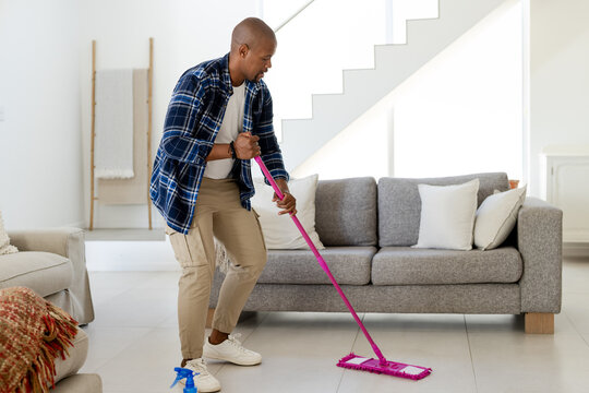 Flat pink mop gliding across tiled floor in modern living room with blue spray bottle
