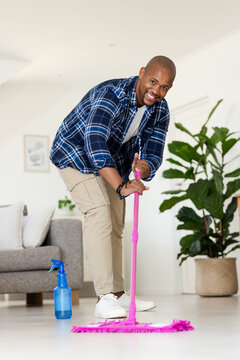 African American man mopping hardwood floor in living room with pink mop, blue bottle, plaid shirt