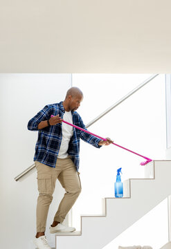 African American man in plaid dusting railing on staircase with pink duster near blue spray bottle
