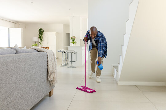 Cleaning man in shirt leaning with pink mop and blue spray bottle, modern home, copy space