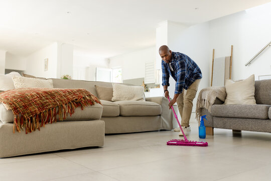 Mopping man in plaid shirt, pushing pink mop by spray bottle in living room, copy space