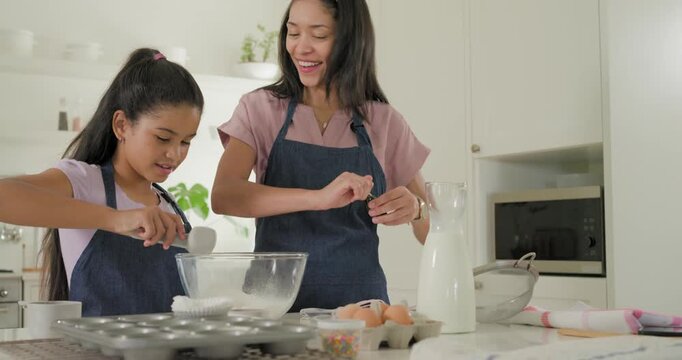 African American mom, teen daughter adding vanilla, eggs into bowl at kitchen counter making batter