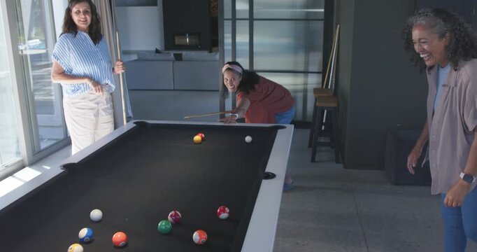 Diverse women in lounge watching center woman lining up, breaking on black felt pool table, playing