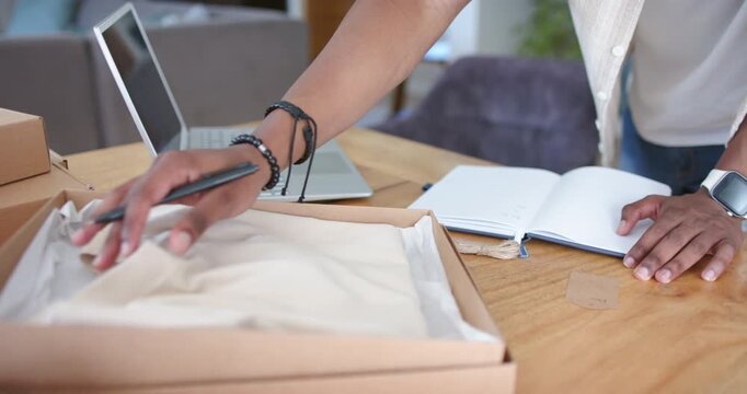 Mature man writing in notebook with pen, inspecting tissue box with garment by laptop, copy space
