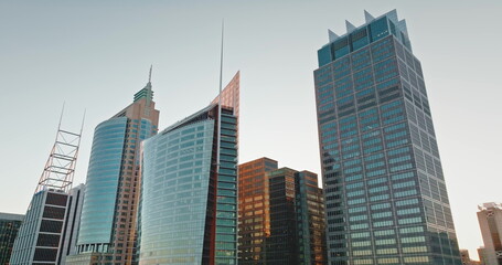 Fototapeta premium Australia, Sydney: Modern glass and steel skyscrapers dominate Sydney skyline, reflecting the warm glow of the sunset sun, creating stunning cityscape architecture background. Drone flight