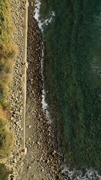 Aerial view of a rocky shoreline and clear turquoise sea with a stone seawall, Acciaroli, Italy. Natural coastal landscape with waves gently lapping the shore.
