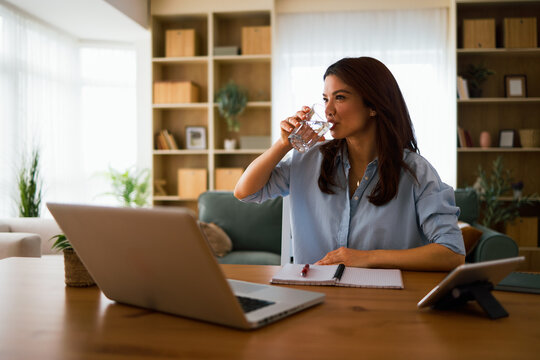 Woman hydrating while working on her laptop from a home office desk