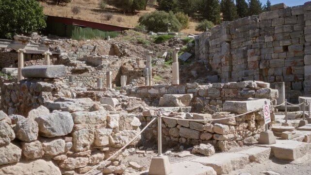 Ancient ephesus ruins with weathered stone walls and scattered columns, defocused foreground and midground in plaza; background backplate copyspace calm.