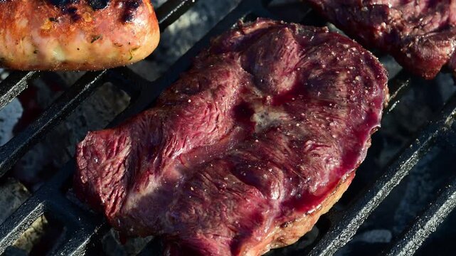 a thick beef steak searing on a hot cast-iron grill, showcasing the glistening surface of the meat and the transition from raw red to a savory browned crust alongside a sizzling Balkan sausage.