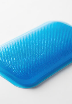 Blue rectangular cooling gel patch with textured surface on white background under soft studio light, calming clinical compress