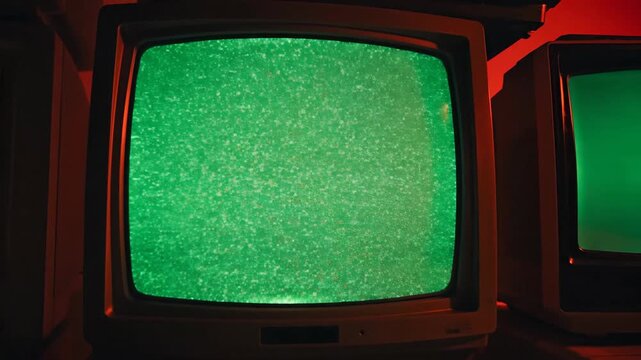 Stack of old televisions with green screens against vibrant red backdrop
