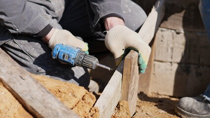 Power Tool Fastening. Handheld Device Driving Screw Into Temporary Concrete Mold Structure. Gloved Hands Operating Cordless Drill To Fasten Formwork During Construction Process © bisonov
