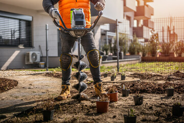 Gardener using tools hand-held soil hole drilling machine or portable manual cordless earth auger for prepare the soil for planting plants. © Peter
