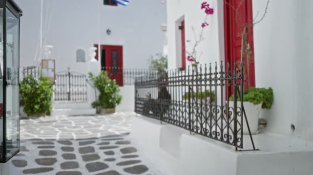 Defocused mykonos street scene with soft bokeh, whitewashed facades, red doors and patterned stone paving street; background backplate copyspace calm.