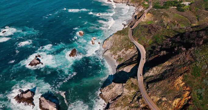 Winding coastal road on edge of steep cliff. Aerial view of Highway 1 curving along the rocky pacific shore with sea stacks in Big Sur, California.