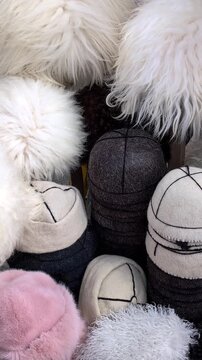 Traditional caucasian papakha fur hats at a local market displaying ethnic headwear for sale, with felt and wool caps alongside fluffy karakul headpieces