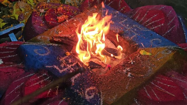 Close-up of a sacred Hindu havan (yajna) ritual with bright flames rising from a decorated fire altar. The scene captures traditional offerings, sacred powders, and ritual elements used in (puja)