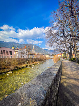 River Eisack flowing through Bressanone with historic town buildings, snowy mountains, and tranquil Parco Rapp