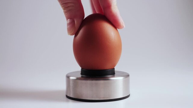 A hand holds a chicken egg and carefully pierces the shell using an Egg piercer, egg pricker. The small hole helps prevent cracking during boiling and makes peeling easier after cooking. High quality