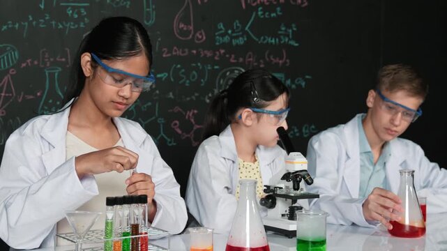 Smart teenager drop sample in microscope while girl inspect carefully at blackboard with chemistry theory. Professional scientist pour chemical product in tube and prepare for experiment. Edification
