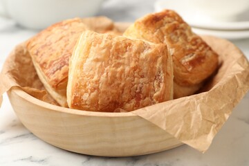 Obraz premium Tasty puff pastries in wooden bowl on white marble table, closeup