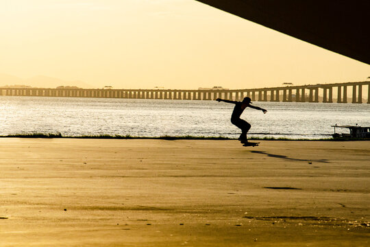 Backlit image of a skateboarder at dusk performing a trick near a lagoon. The scene evokes skateboarding culture as a contemporary expression in dialogue with the landscape of Rio de Janeiro.