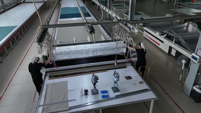 Automated quilting machine sewing fabric at a modern textile factory, overhead drone shot
