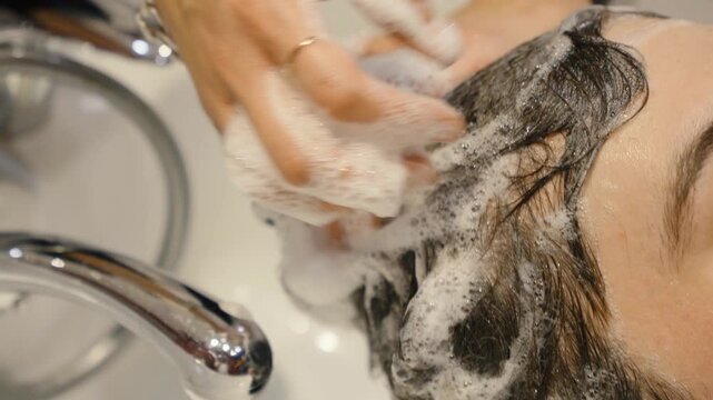 Hand massaging soapy hair of a client in a wash basin
