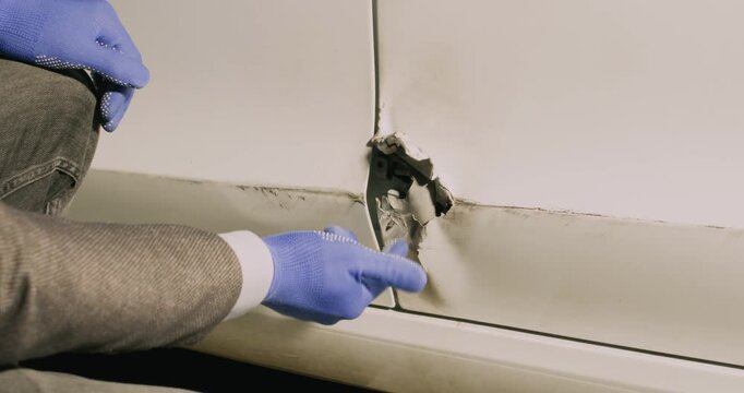 Insurance inspector hands examine hole in car door at service station closeup. Skilled agent looks for signs of vehicle intentional damage in parking lot
