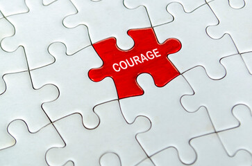 Fototapeta premium COURAGE, Single red courage puzzle piece positioned alone in the center of a white interlocking jigsaw puzzle surface