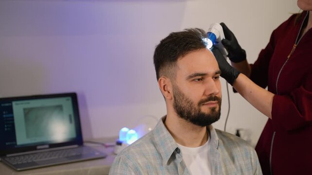 Trichologist examining man's hair and scalp with dermatoscope