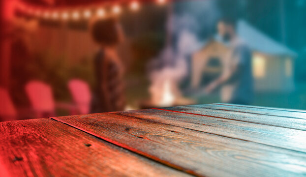 Empty wooden table with clear copy space for product placement in a garden environment. Blurred background of cozy outdoor scene with greenery and barbecue elements.  Grilling, dining and relaxation.