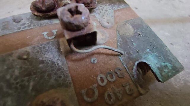 Macro shot of a corroded water heater electrical connector with heavy rust and green oxidation. Close-up view highlights damaged terminals and resistance markings on a weathered metal surface.