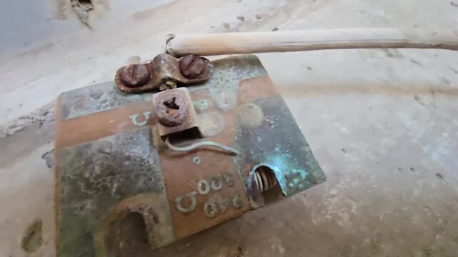 Macro shot of a corroded water heater electrical connector with heavy rust and green oxidation. Close-up view highlights damaged terminals and resistance markings on a weathered metal surface.