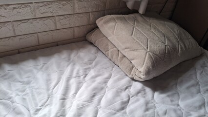 Fototapeta premium Comfortable bedroom setup featuring a soft beige textured pillow on a clean white quilted mattress pad.
