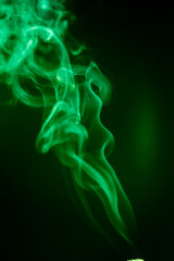Obraz premium Elegant swirling green smoke against a dark backdrop, creating an abstract and mysterious aesthetic. The smoke rises gracefully, showing captivating textures and forms